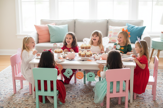 Costumed children laughing around a decorated Halloween party table with cupcakes and pumpkins